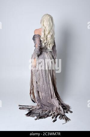 Ritratto di bionda ragazza che indossa strappato vecchio abito da sposa a lunghezza intera in piedi posa, isolato contro uno sfondo studio. Foto Stock