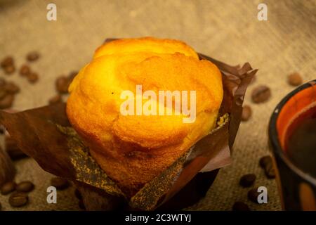 Cupcake fresco, tazza di caffè e chicchi di caffè su un tessuto casalinga con una consistenza ruvida. Primo piano Foto Stock