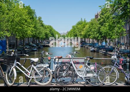 Canale Keizersgracht alberato nel centro di Amsterdam con biciclette parcheggiate contro la ringhiera e persone su una barca che naviga lungo il canale. Foto Stock