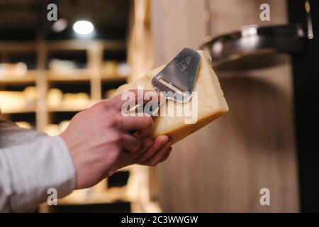 Uomo affettare un pezzetto di formaggio per il gusto. Giovane lavoratore utilizzare coltello speciale per il formaggio Foto Stock