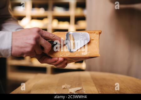 Uomo affettare un pezzetto di formaggio per il gusto. Giovane lavoratore utilizzare coltello speciale per il formaggio Foto Stock