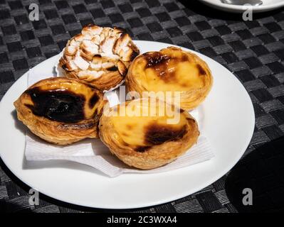 Crostate tradizionali portoghesi, Pastéis de Nata e crostata di mandorle su piatto bianco. Sono croste croccanti, sfoglia di pasta sfoglia ripieni di crema al forno Foto Stock