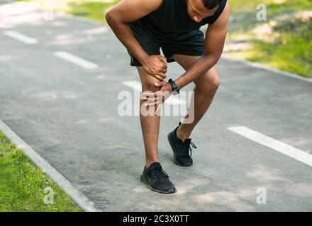 Jogger afro-americano che soffre di dolore al ginocchio durante la sua corsa mattutina al parco Foto Stock