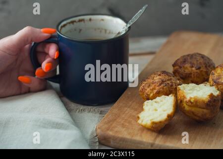 La ragazza beve caffè da una grande tazza blu con muffin. Sfondo della colazione Foto Stock