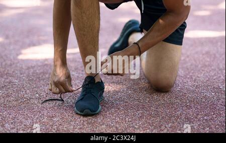Giovane sportivo che legava le scarpe durante la sua mattina corre all'aperto, vicino alle gambe Foto Stock