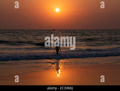 Silhouette di una giovane donna al tramonto in acqua a Majorda spiaggia a Goa, India Foto Stock