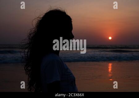 Profilo silhouette di giovane donna al tramonto sulla spiaggia di Majorda a Goa, India. Foto Stock