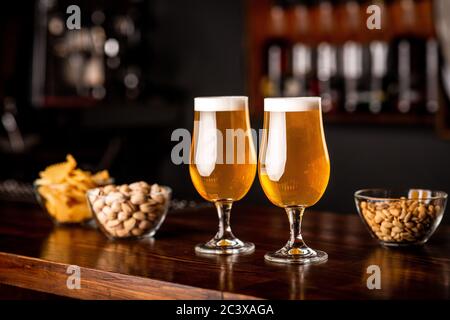 Spuntini nel pub su un bar di legno. Due bicchieri con birra, patatine, noci e pistacchi Foto Stock