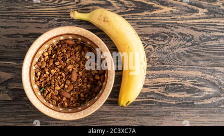 Granola fatta in casa con noci in una ciotola marrone e banana. Colazione deliziosa e abbondante. Tavolo rustico in legno Foto Stock