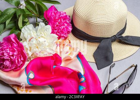 Bouquet di fucsia e di pony bianco, cappello di paglia con nastro nero, sciarpa di seta e occhiali da sole su sfondo lilla. Primo piano, piatto Foto Stock