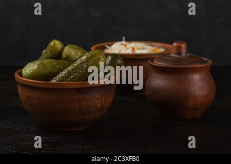 Cetrioli e crauti in una ciotola di argilla su fondo di cemento scuro Foto Stock