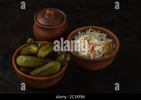 Cetrioli e crauti in una ciotola di argilla su fondo di cemento scuro Foto Stock