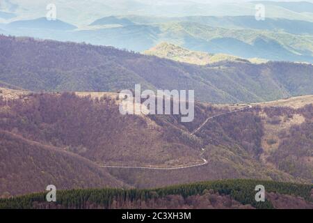 Strada di montagna curvy che conduce alla cima della collina, pineta di primo piano e strati di montagna di sfondo Foto Stock