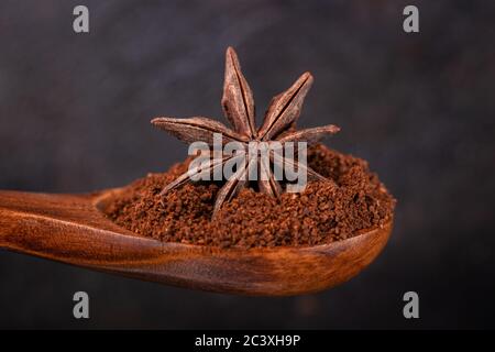 Anice stellato in un cucchiaio di legno con caffè macinato su sfondo scuro Foto Stock