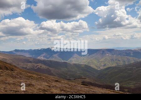 Vista panoramica di incredibili strati di montagna illuminati da luce soffusa, soffici nuvole bianche su un cielo blu e fiori di zafferano in primo piano Foto Stock