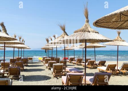 Le file di lettini vuoti con ombrelloni in spiaggia. Cielo blu e mare turchese. Giornata estiva soleggiata. Vlora / Vlore, Albania, Europa. Foto Stock