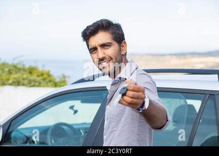 Ritratto closeup felice, sorridente, giovane uomo, acquirente mostrando le chiavi della sua nuova auto isolato al di fuori del lotto della concessionaria. Trasporto personale, acquisto auto Foto Stock