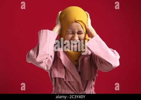 Ragazza teenage musulmana asiatica che indossa hijab, urlando che perde temperamento, cant controllo emozioni, occhi vicini e orecchie mentre urla, su sfondo rosso Foto Stock