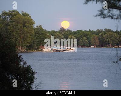 Luna Rising attraverso le nuvole rosa sopra un lago Foto Stock