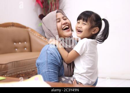 Madre musulmana che indossa hijab sorridente mentre gioca con la sua bambina, mamma e figlia si amano l'un l'altro, felice singolo genitore Foto Stock