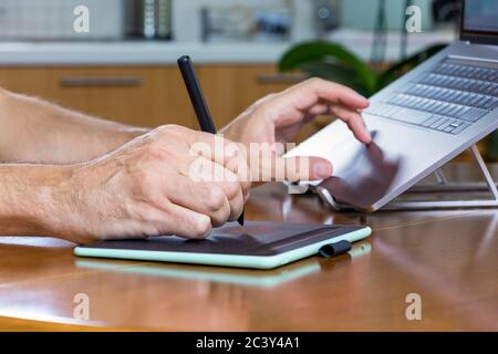 Il designer maschile lavora a casa utilizzando un tablet grafico e un notebook Foto Stock