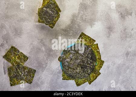 Nori croccanti alghe in una ciotola blu su sfondo grigio. Cibo giapponese nori. Fogli secchi di alghe. Disposizione piatta. Spazio di copia Foto Stock