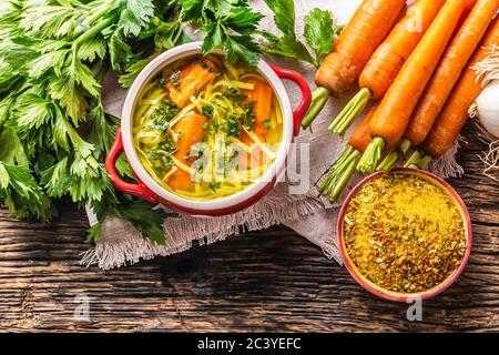 Brodo zuppa di pollo in una ciotola vintage con tagliatelle fatte in casa carota cipolla sedano erbe aglio e verdure fresche. Foto Stock
