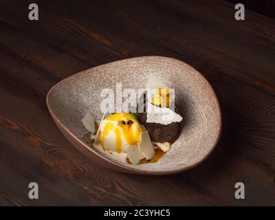Brownie al cioccolato caldo servito con una tazza di gelato, foglie di menta e guarnito con frutti di bosco e fiori. Su uno sfondo di legno da abbandonato Foto Stock