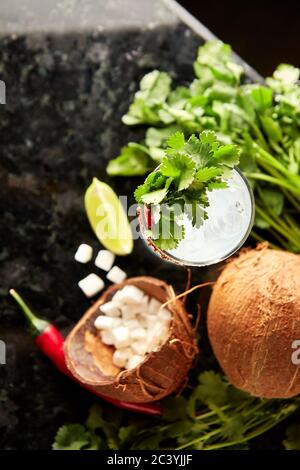 Cocktail con rum, sciroppo di cocco, coriandolo, lime e peperoncino rosso sul banco bar in marmo nero Foto Stock