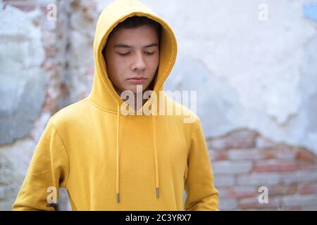 un adolescente in una felpa gialla guarda giù Foto Stock