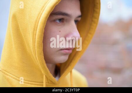 un adolescente in una felpa gialla guarda di fronte lui Foto Stock