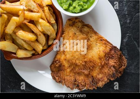 Una porzione di pesce e patatine cucinate in casa con piselli. Il pesce è un'ala fritta e martellata da un raggio di spina, Raja clavata, e le patatine sono Foto Stock