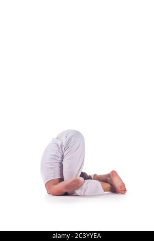 Uomo che pratica yoga facendo la ' ginocchio all'orecchio posa ' su sfondo bianco. Karnapidasana. Foto Stock