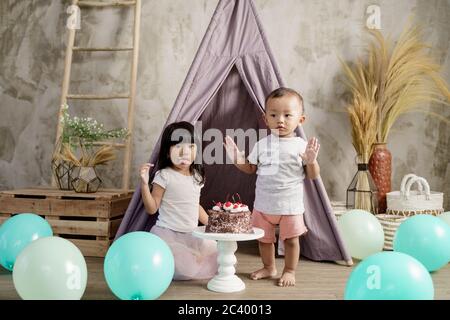 la bambina tirò fuori la lingua sfregando la crema sulle labbra e il fratellino sollevò le mani felicemente durante la festa di compleanno Foto Stock