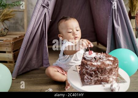 piccolo ragazzo asiatico cercando di raccogliere le ciliegie sulla torta di compleanno Foto Stock