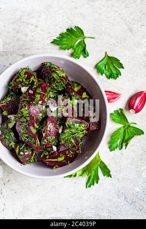 Insalata di barbabietole con aglio ed erbe in un recipiente grigio su sfondo chiaro. Foto Stock