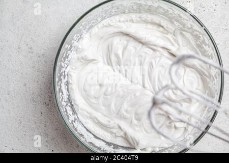 Cottura della panna per la torta in un recipiente di vetro e in un mixer. Panna bianca montata. Panna di cocco montata per torta vegana, vista dall'alto. Foto Stock