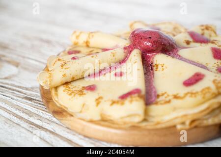 Colazione con pancake caldi e gelato alla fragola. Pancake delicati e deliziosi su un piatto di legno con marmellata rossa Foto Stock