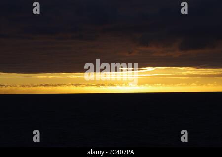 Tramonto su nuvole scure e mare, fascio luminoso di orizzonte tra nuvole scure e mare, sequenza di immagini di tramonto che emergono dal cielo scuro Foto Stock