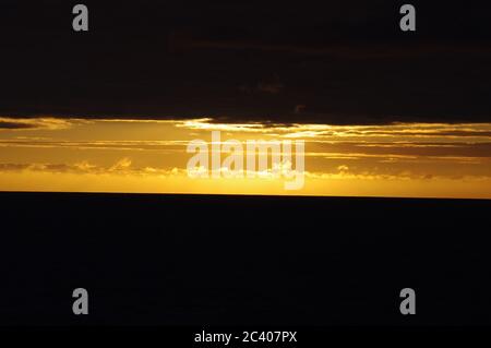 Tramonto su nuvole scure e mare, fascio luminoso di orizzonte tra nuvole scure e mare, sequenza di immagini di tramonto che emergono dal cielo scuro Foto Stock