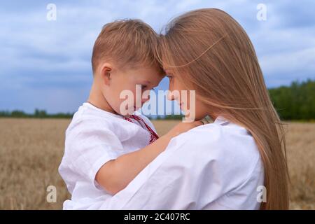 Ritratto di un figlio allegro con una macchina fotografica seduta sulle mamme che si trova in mezzo al campo di grano. Foto Stock