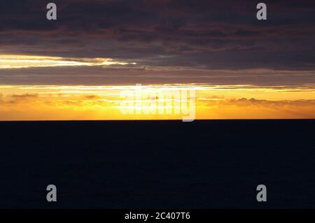 Tramonto su nuvole scure e mare, fascio luminoso di orizzonte tra nuvole scure e mare, sequenza di immagini di tramonto che emergono dal cielo scuro Foto Stock