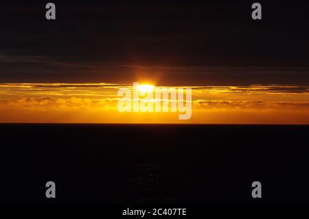 Tramonto su nuvole scure e mare, fascio luminoso di orizzonte tra nuvole scure e mare, sequenza di immagini di tramonto che emergono dal cielo scuro Foto Stock