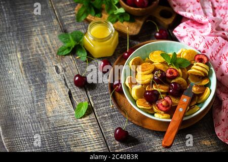 Colazione con minuscoli pancake. Mini frittelle con ciliegie e miele su rustico tavolo di legno. Spazio di copia. Foto Stock
