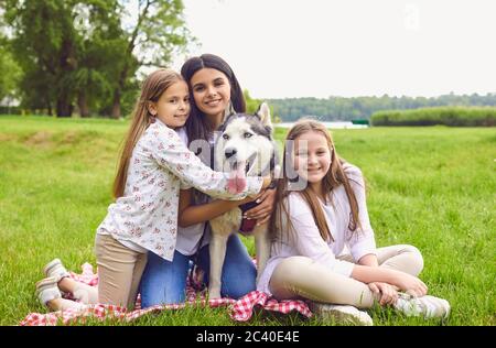 Ritratto di una madre e di due figlie con un cane Husky sorridente guardando la macchina fotografica in un parco estivo. Foto Stock