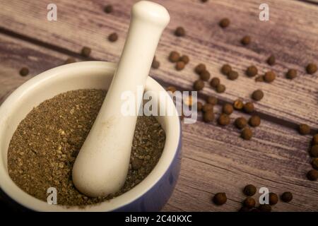 Allspice in un mortaio di ceramica e allspice sparso su un tavolo di legno. Primo piano Foto Stock