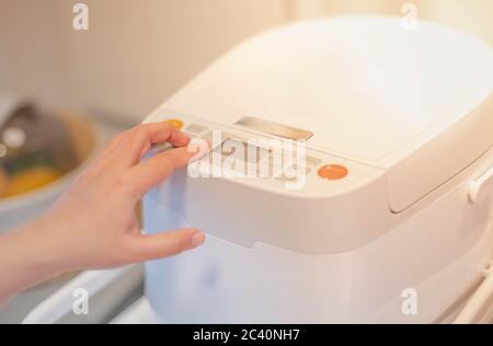 Mano femminile premendo il pulsante del nuovo cuoci riso moderno in cucina preparazione del cuoco per la famiglia, nuova macchina elettronica tecnologia concep Foto Stock