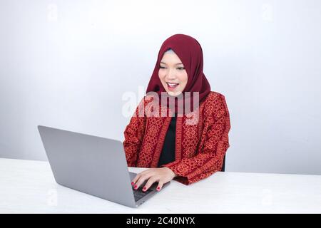 La giovane donna islam asiatica che indossa il copricapo è scioccata ed eccitata con che cosa vede sul laptop sul tavolo. Foto Stock