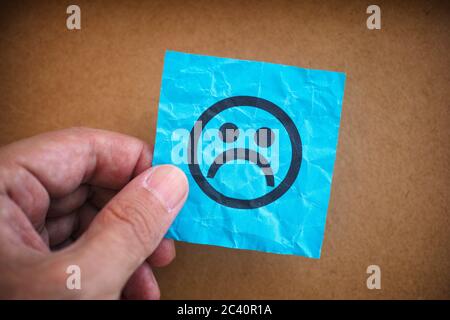 Uomo che tiene una nota di carta blu con il volto triste in mano. Primo piano. Foto Stock