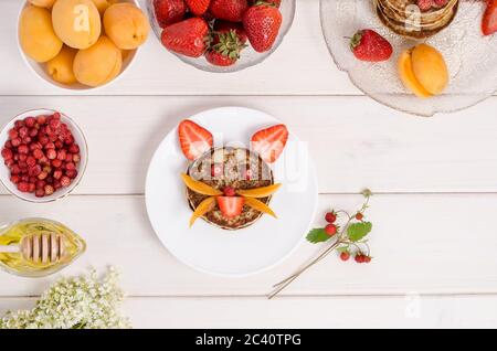 Pancake per la colazione di un bambino sotto forma di viso di gatto fatto di fragole e albicocche da vicino. Gustosa colazione estiva. Foto del cibo. Foto Stock